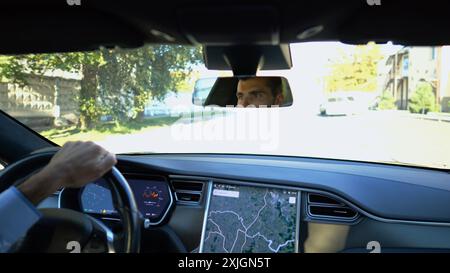 Yeux du conducteur masculin réfléchissant le rétroviseur pendant la conduite d'une voiture électrique. Homme confiant conduisant une voiture moderne en ville. Jeune homme regardant Banque D'Images