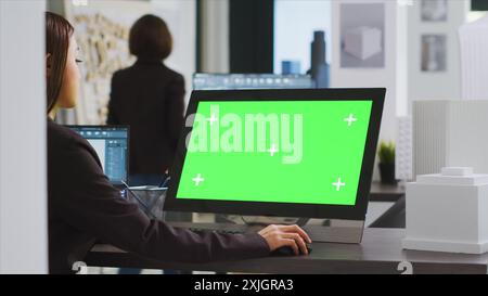 Spécialiste de la CAO utilisant un ordinateur avec écran vert au bureau, examinant l'affichage du pc avec une disposition d'espace de copie isolé dans l'espace de coworking d'affaires UNICORN. Modèle chromakey vierge de l'architecte sur le moniteur. Banque D'Images
