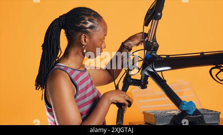 Ingénieur utilise un tournevis pour serrer les vis de leviers de frein sur le guidon de vélo, examinant les composants, fond de studio. Expert dévissant les pièces défectueuses de vélo afin de les remettre en état, studio A. Banque D'Images