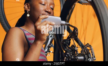 Technicien expérimenté utilisant de la colle spécialisée pour réparer la chaîne de vélo défectueuse, fond de studio orange. Travailleur appliquant de l'adhésif sur les pièces de vélo pendant le processus d'inspection, gros plan Banque D'Images