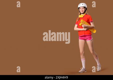 Belle jeune femme dans le casque avec skateboard sur fond brun Banque D'Images