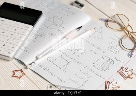 Copybook avec formules mathématiques manuscrites, calculatrice et papeterie sur fond de bois blanc Banque D'Images