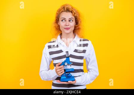Une femme professeur de biologie scolaire tient un microscope. Femme professeur de biologie. Professeur avec microscope isolé sur jaune. Sciences biologiques pour la femme Banque D'Images