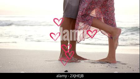 Image de cœurs se déplaçant sur les jambes d'un couple diversifié amoureux sur la plage en été Banque D'Images