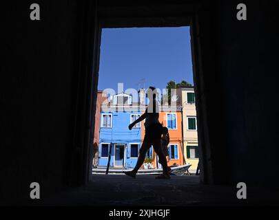 Venise, Italie. 18 juillet 2024. Une femme passe devant les maisons colorées de l'île de Burano, Venise, Italie, 18 juillet 2024. Crédit : Alberto Lingria/Xinhua/Alamy Live News Banque D'Images