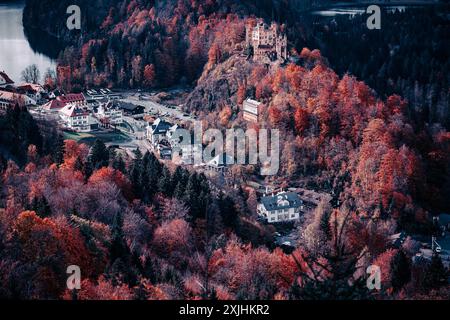 Vue aérienne du château de Neuschwanstein niché au milieu du feuillage d'automne, avec un village voisin et un lac. Banque D'Images
