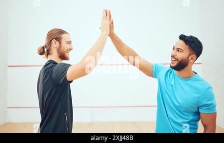 Sportifs, heureux et les hommes avec High Five pour la collaboration, l'entraînement et l'entraînement pour le jeu de squash. Sourire d'équipe, athlètes et connexion de paume pour Banque D'Images