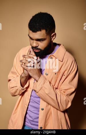 Un bel homme afro-américain en tenue à la mode est profond dans le geste de prière. Banque D'Images