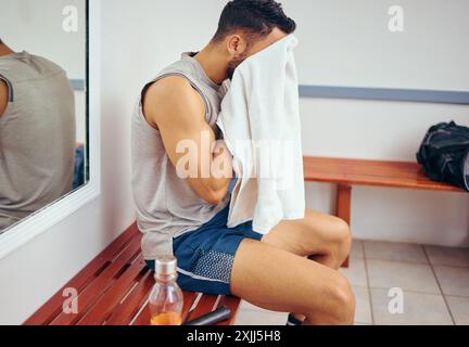 Homme, fitness et serviette avec visage pour la pause, le repos ou la récupération de la sueur, l'entraînement ou l'entraînement dans le vestiaire au gymnase. Jeune homme essuyant sur le banc Banque D'Images