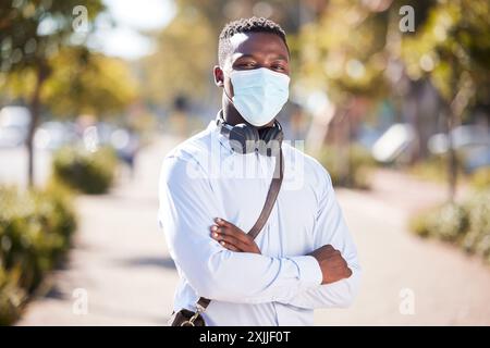 Bras croisés, masque et portrait d'homme d'affaires en plein air dans le parc pour le trajet matinal au travail. Confiant, covid et écouteurs pour la musique avec Banque D'Images