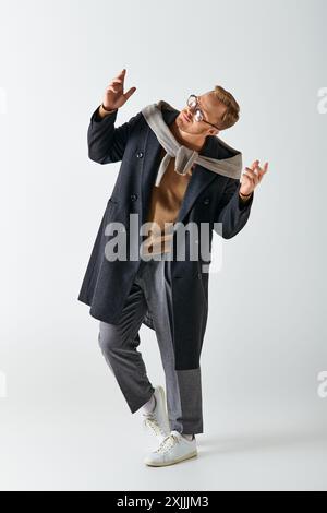 Un homme élégant dans un manteau et des lunettes danse énergiquement. Banque D'Images