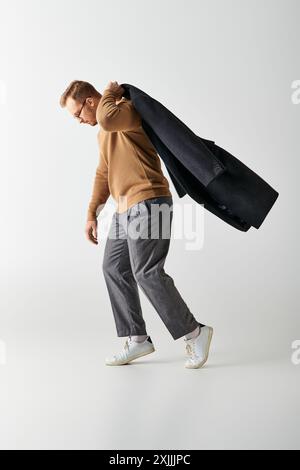 Un homme à la mode dans des vêtements élégants marchant énergiquement tout en portant un manteau. Banque D'Images