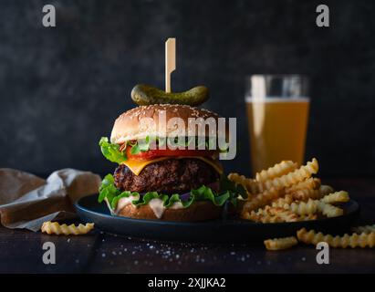 Hamburger, frites et bière sur table en bois avec fond sombre. Banque D'Images