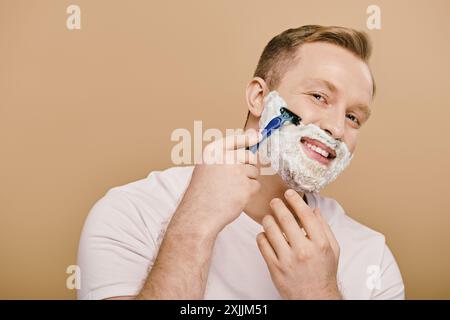 Un homme suave en tenue décontractée effectue sa routine de soins de la peau, rasant habilement son visage avec un rasoir. Banque D'Images