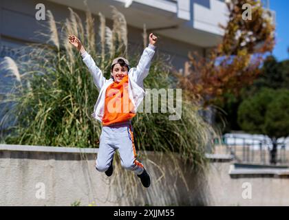 mignon garçon en t-shirt orange sauté avec les mains levées vers le haut Banque D'Images