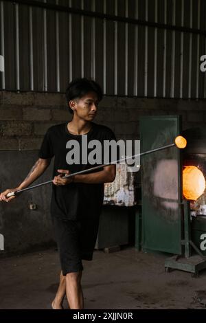 L'homme travaillant avec le verre fondu à l'aide d'une pincette dans une usine de verre Banque D'Images