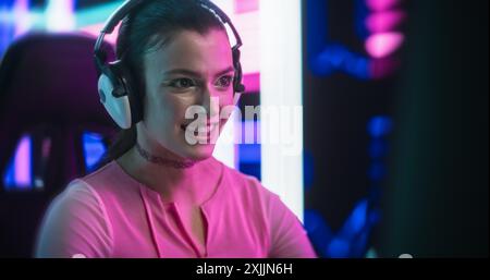 Jeune femme élégante jouant à des jeux vidéo sur un ordinateur de bureau dans une salle technologiquement avancée avec fond de néon futuriste. SCI-Fi, Cyber Technology et concept pour les amateurs de jeux Banque D'Images