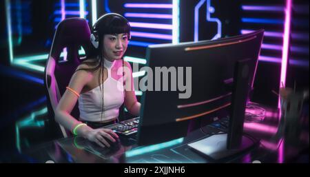 Jeune joueur en ligne jouant à un jeu vidéo dans une salle cyberpunk futuriste. Cosplay Girl utilisant des écouteurs, parler avec des joueurs pendant le flux de jeu. Pro Gamer remportant une manche intense et célébrant Banque D'Images