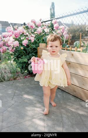 Petite fille avec arrosoir rose dans un jardin, entourée de fleurs Banque D'Images