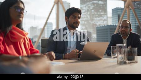 Portrait d'un jeune administrateur prospère faire un rapport à un conseil d'administration lors d'une Assemblée financière annuelle dans la salle de conférence. Des gens d'affaires et des partenaires discutent du travail dans un bureau Banque D'Images