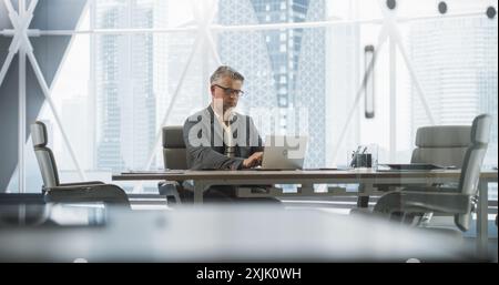 Portrait d'homme d'affaires caucasien prospère travaillant sur ordinateur portable dans son bureau Big City Corner. Professionnel homme Digital entrepreneur fait l'analyse de données pour l'évaluation de stratégie de commerce électronique. Banque D'Images