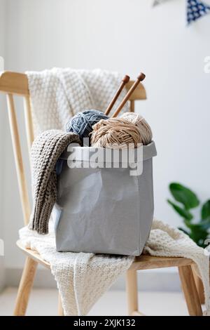 Fils de fil avec des aiguilles à tricoter dans un sac artisanal debout sur une chaise en bois Banque D'Images