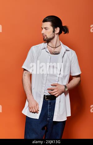 Bel homme caucasien se tient confiant sur fond orange vif, chemise blanche sportive à la mode. Banque D'Images