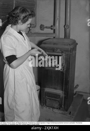 Vivre dans les années 1940 Une jeune femme travaillant comme femme de ménage et le photographe la suivaient pendant une journée de travail, en commençant par elle dans la cave de la maison, faisant un feu dans la chaudière. Suède 1940. Kristoffersson ref 55-6 Banque D'Images