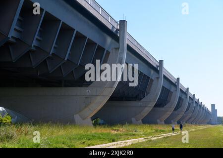 19 juillet 2024, Saxe-Anhalt, Wolmirstedt : les marcheurs marchent le long du pont du canal de Magdebourg. Le pont du canal de Magdebourg se compose du pont avant-pays de 690 mètres de long et du pont fluvial de 228 mètres de long. Au total, le pont canal mesure 918 mètres de long, ce qui en fait le plus long pont canal au monde. Il transporte le trafic maritime du canal Mittelland à travers l'Elbe. La forme des piliers du pont de l'estran est destinée à ressembler aux côtes d'un navire. La structure fait partie de l'intersection de la voie navigable de Magdebourg. Environ 68 000 mètres cubes de béton armé étaient Banque D'Images