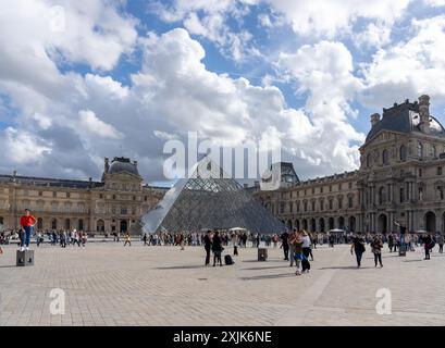 Paris, France - 19 octobre 2023 : la pyramide de verre du Musée du Louvre se détache sur le ciel nuageux à Paris, France. Les touristes se promènent à travers Banque D'Images