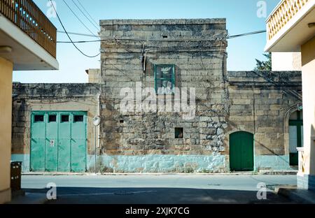 Ancien bâtiment en pierre avec portes vertes et fenêtre, situé dans une rue calme sous un ciel bleu clair. Architecture historique. Banque D'Images