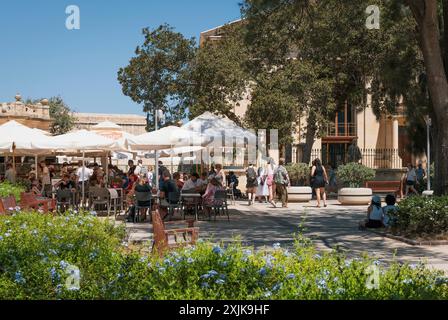 Un café en plein air animé dans un parc urbain rempli de gens profitant d'une journée ensoleillée. Les arbres et les fleurs créent un environnement serein. Banque D'Images