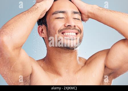 Homme heureux, soins capillaires et douche pour le traitement en studio, dermatologie et eau sur fond bleu. Personne masculine, toilettage et shampooing de luxe pour Banque D'Images