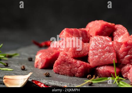 Dés de viande de bœuf en cubes sur planche de pierre avec thym et poivrons Banque D'Images