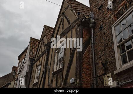 Une rangée de bâtiments historiques à colombages avec des murs en briques et en plâtre, avec des toits à pignons et des poutres en bois. Le ciel est couvert, ajoutant un a de humeur changeante Banque D'Images