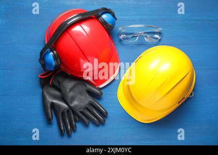 Casques de sécurité, gants de protection, protections auditives et lunettes sur fond de bois bleu, pose à plat Banque D'Images