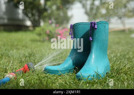 Bottes en caoutchouc brillantes sous pression de l'eau sur l'herbe verte à l'extérieur Banque D'Images