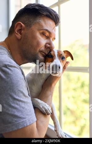 Adorable homme et adorable, joli chiot Jack Russel terrier près de la fenêtre. Gros plan, intérieur. Lumière du jour. Concept de soins, d'éducation, d'obéissance trainin Banque D'Images