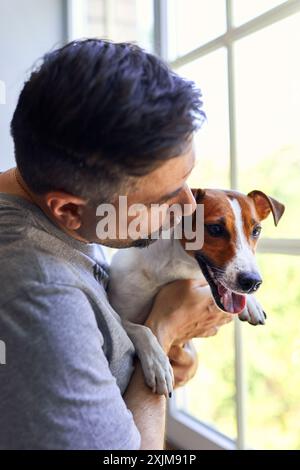 Adorable homme et adorable, joli chiot Jack Russel terrier près de la fenêtre. Gros plan, intérieur. Lumière du jour. Concept de soins, d'éducation, d'obéissance trainin Banque D'Images