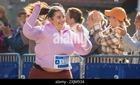 Portrait d'une coureuse féminine plus Size souriante traversant la ligne d'arrivée et démontrant sa volonté. Le public du marathon de la ville sympathique est favorable Banque D'Images
