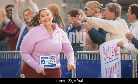 Portrait d'une coureuse féminine plus Size souriante traversant la ligne d'arrivée et démontrant sa volonté. Le public du marathon de la ville sympathique est favorable Banque D'Images