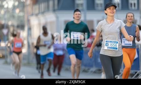 Groupe souriant de personnes participant à un marathon de la ville. Divers coureurs de course atteignant la ligne d'arrivée, célébrant leur victoire et atteignant leur objectif Banque D'Images