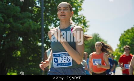 Portrait d'une femme qui court et participe à un marathon dans un parc. Strong Athletic Female Jogger Racing autres coureurs avec détermination pour la première place dans la ligne d'arrivée Banque D'Images