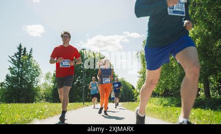 Portrait d'un groupe de personnes participant ensemble à un marathon et courant à travers un sentier de parc. Joggers donnant de leur mieux pour atteindre la ligne d'arrivée dans une course amicale Banque D'Images