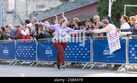 Portrait d'une coureuse féminine plus Size souriante traversant la ligne d'arrivée et démontrant sa volonté. Le public du marathon de la ville sympathique soutient les participants de haut niveau Banque D'Images