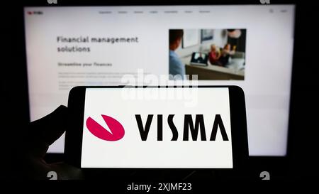Stuttgart, Allemagne, 06-12-2022 : personne tenant un téléphone portable avec le logo de la société norvégienne de logiciels Visma COMME sur l'écran en face de la page Web de l'entreprise. Banque D'Images