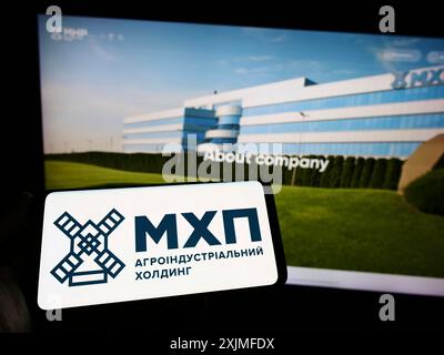 Stuttgart, Allemagne, 06-18-2022 : personne tenant un smartphone avec le logo de la société ukrainienne Myronivsky Hliboproduct (MHP) sur l'écran devant le site. Banque D'Images