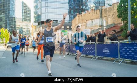 Portrait d'un homme d'âge moyen souriant qui court dans un marathon de ville, agitant devant le public de soutien. Amical Happy Male Runner célébrant le franchissement de la ligne d'arrivée dans une course Banque D'Images