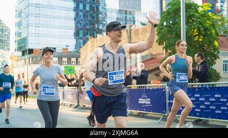 Portrait d'un homme d'âge moyen souriant qui court dans un marathon de ville, agitant devant le public de soutien. Amical Happy Male Runner célébrant le franchissement de la ligne d'arrivée dans une course Banque D'Images