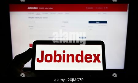 Stuttgart, Allemagne, 07-03-2022 : personne tenant un téléphone portable avec le logo de la société danoise de plate-forme de recrutement jobIndex COMME sur l'écran en face de la page web. Banque D'Images